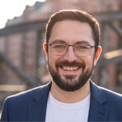 Portrait of Jonas Janz smiling, in a navy blazer, in Hamburg's Speicherstadt